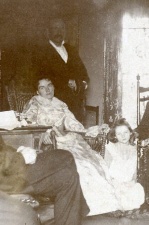 A woman sitting in a chair with a man standing behind her and a little girl sitting at her feet