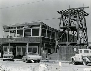 A two-story building with cars parked in front beside a large water tower that is under construction