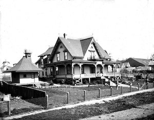 A large Victorian home with a wrap-around porch and a small building in the yard