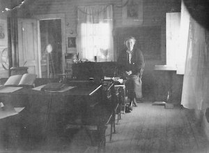 Woman standing in a classroom featuring desks, books and chalkboard