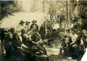A large group of people in the woods with a tent behind them