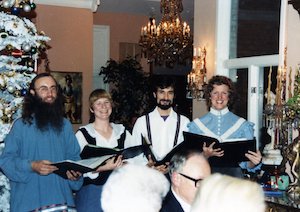 Two men and two women holding open choir books next to a Christmas tree