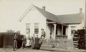 A family posing in front of a home with shrubs and a wooden fence in front