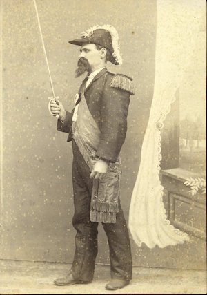 Studio portrait of a man with shoulder tassels, a large sash, and bicorne hat holding a drawn sword