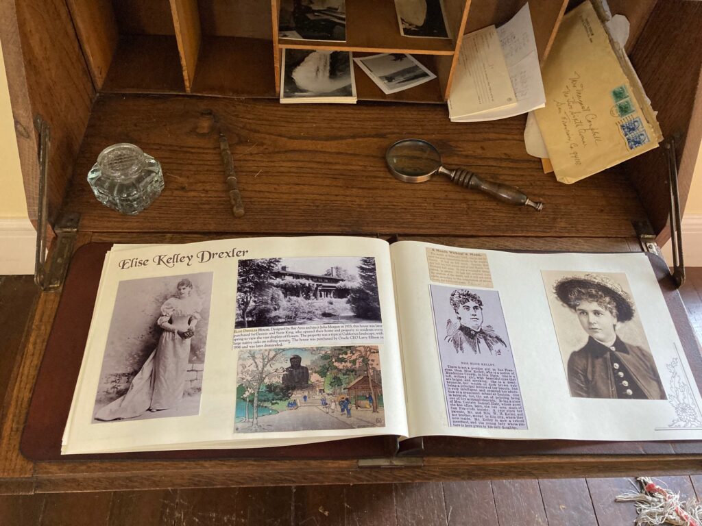 An opened scrapbook of Elise Kelley Drexler sitting on a desk with letters, photos, inkwell and magnifying glass