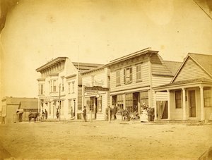 Buildings along a dirt street with people in front of them