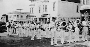 A uniformed marching band with instruments standing in a building-lined street