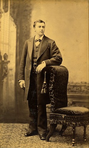 Studio portrait of Victorian young man in a suit leaning against a chair