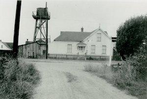 House with water tower next to it at end of dirt drive