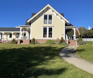 Side of a large house with porches on front and back side in a grassy yard