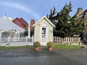 Small wooden building in front of a fenced in yard and buildings