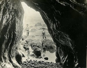 View from inside a cave of a man and child standing in front of the ocean 