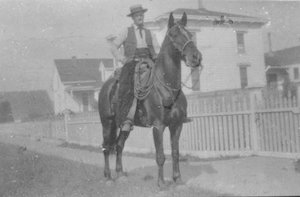 Man on horseback with fence and building behind him