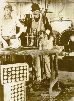 Two men in a factory standing behind a table full of bottles