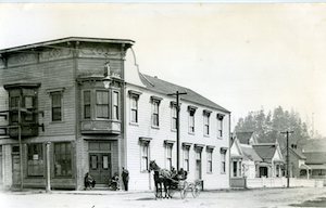 Two-story building on a street corner with horse-drawn carriage in front
