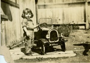 Young boy standing beside a older-style toy car