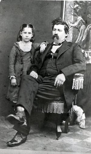 Seated man in a suit with a young girl leaning against him