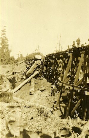 Wreckage with train coming off raised wooden railroad tracks