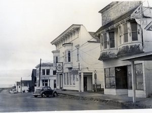 Main Street, Mendocino, 1966, near the corner of Main and Kasten Streets, looking west. A Volkswagen Bug automobile is parked on the street. 

Behind it is the Bank of America in the two-story white structure on the west side of Kasten. Dostal's Clock Shop (note sign) occupies the Jarvis & Nichols Building on the east side of Kasten Street, with the second-story bay windows. Zacha's Bay Window Gallery is entered through its corner doorway. The building in the right foreground was at one time the Remedy Store, Mendocino's local drug store and soda fountain, and then became Shrode's Sundries until 1963. Note the corrugated metal siding on this building. (Kelley House Collection, Kelley House Photographs)
