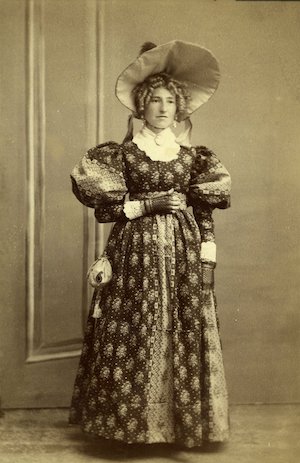Portrait of a standing woman in a patterned dress and large hat