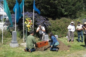 People gathered in a cemetery burying a small wooden box 