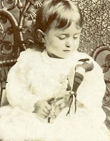 Well-dressed toddler posing in a chair holding a toy parrot