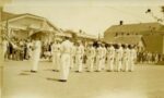 I.D.E.S. Drill Team, 1925 - 1933. Photograph of I.D.E.S. (Irmandade di Espirito Santo, Brotherhood of the Holy Ghost), a Portuguese men's organization. In 1910 the membership roster noted there were 73 members. This organization had its own marching band and drill team, as shown in the picture. They are standing on Main Street in Mendocino in front of Dr. Carl Vincent Whited's bungalow-style home and office (flat roof to the right) located where the Alhambra Hotel used to be, east of the Mendocino Hotel. The long 2-story building on the far right is Joseph Heisel’s shoe store. Between 1895 and 1897, this structure housed the Mendocino Hospital & Drug Company. The building was demolished in 1941.