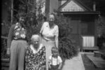 Four Generations of the Flood-Escola Family in Mendocino, 1948. Four generations starting with Rose Watkins Flood, who is seated in this photo. Standing behind Rose, on the right, is Rose’s daughter, Nannie Flood Escola, and on the left, is Nannie’s daughter, Dorothy Escola Schlafer. Dorothy's son (Rose’s great-grandson) Steve Schlafer, standing in front. Photograph taken in 1948 at the Flood home in Mendocino, located on Pine Street. In 1964, the house was moved easterly on the lot by CalTrans to make way for the new Big River bridge approach, cutting off a portion of the westerly end of the parcel. (Gift of Linda Mechling, The Nannie Escola Collection, Kelley House Photographs)