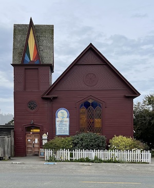 Former church painted dark red with large glass window and side tower