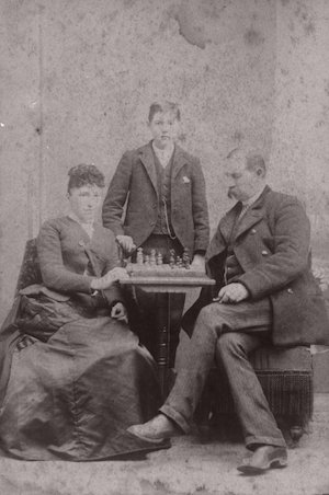 Three teens posed around a chess board