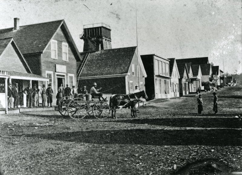Dirt road lined with buildings and horse-drawn cart